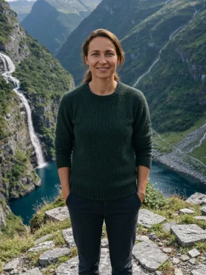 Lena on a rocky ledge above a fjord, with a waterfall down the steep green slopes